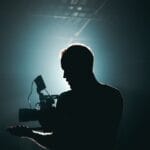 Silhouette of a cinematographer with camera gear in a dramatic, low light setting.